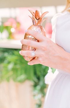 a pregnant woman holding a pineapple shaped glass bottle in her right hand and wearing a diamond ring