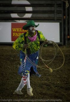 a man in a green hat holding a lasso while standing on top of a grass covered field