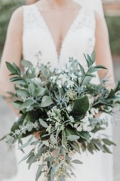 a bride holding a bouquet of flowers and greenery