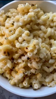 a white bowl filled with macaroni and cheese on top of a marble table