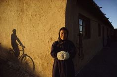 a woman standing in front of a building with a bike parked next to her on the side