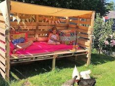 a child laying on a bed made out of wooden pallets in the grass with chickens nearby