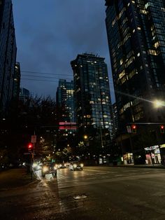 cars driving down the street at night in front of tall buildings with lights on them