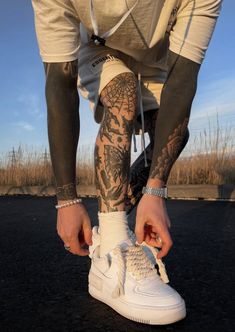 a man with tattoos on his arm and leg is tying up white sneakers in the street