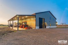 a large metal building sitting on top of a dirt field next to a green tractor