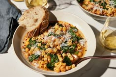 pasta with spinach and parmesan cheese in a bowl next to two glasses of wine