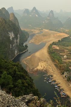 boats are parked on the river bank near mountains and valleys in an area that is surrounded by greenery