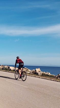 a man riding a bike down the middle of a road next to the ocean on a sunny day