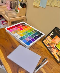 a wooden table topped with lots of paint and a tablet computer next to it on top of a wooden desk