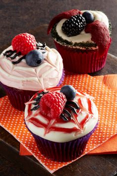 two cupcakes with white frosting and berries on top are sitting on an orange napkin