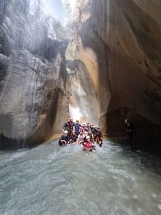 a group of people standing in the middle of a river next to a large waterfall