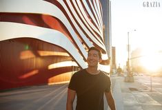 a man standing in front of an american flag on the side of a building with his hands in his pockets