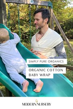 A father using The Simply Pure Organic Cotton Baby Wrap to hold their baby up while supervising his other child go down a playground slide.