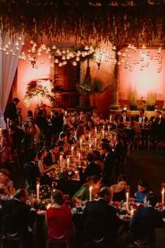 a group of people sitting at tables with candles in front of them and lights hanging from the ceiling