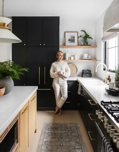 a woman standing in a kitchen next to a stove top oven and countertop with potted plants on it