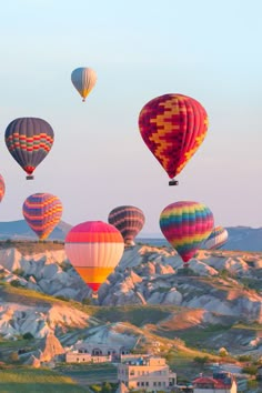 many hot air balloons are flying in the sky over some hills and houses, while another balloon is above them