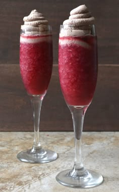 two wine glasses filled with red liquid and whipped cream