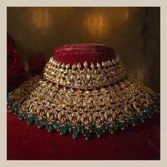 a gold choker with green and red stones on the neck, surrounded by flowers