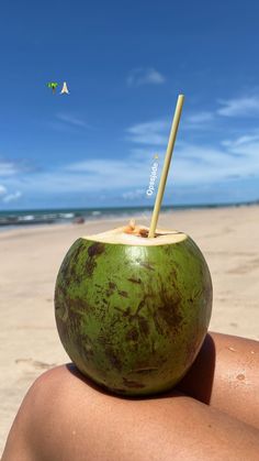 a person sitting on the beach with a coconut drink in their hand