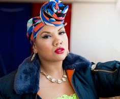 a woman wearing a colorful head scarf and holding her hand out to the side while looking off into the distance