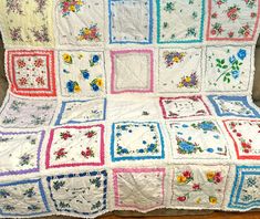 a white quilt with flowers on it sitting on top of a wooden floor next to a chair