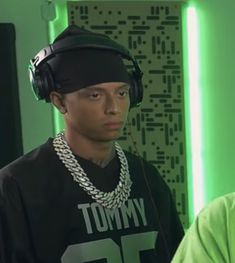 a young man wearing headphones standing in front of a green wall with lights behind him