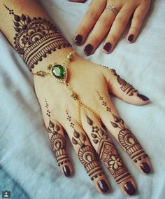 a woman's hand with henna tattoos and jewelry on it, sitting on a bed