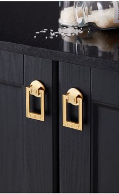 a black cabinet with two gold handles and an empty bottle on the counter top next to it