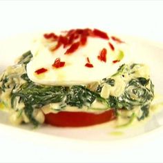 a white plate topped with food covered in sauce and spinach on top of it