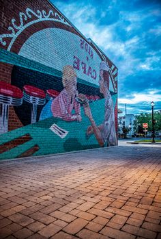 a mural painted on the side of a building in front of a brick sidewalk and street