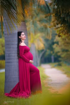 a pregnant woman in a red dress leaning against a palm tree and posing for the camera