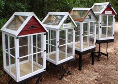 four small greenhouses are lined up on the ground in front of some trees and bushes