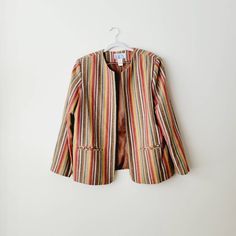 Fun rainbow vertical striped blazer jacket, fully lined with two front pockets. 75% polyester, 25% wool. The texture and colors of the fabric look like linen. Vertical stripes in varying sizes of red, pastel blue, yellow, pink, purple, gray, white, aqua blue, and oatmeal. Tag reads size 18. Fits like large/extra large. 17 inches shoulder to shoulder seam. 23 inches across the bust. 28 inches top of shoulder to bottom hem. 23.5 inches sleeve to shoulder seam. Colorful Business Casual, Red Pastel, Spring Blazer, Vintage Rainbow, Striped Jacket, Striped Blazer, Purple Gray, Vertical Stripes, Kentucky Derby