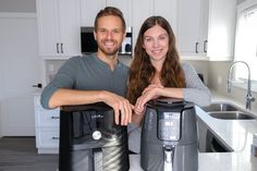 a man and woman standing in front of two large coffee makers on a kitchen counter