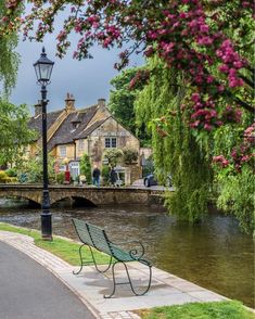 a bench sitting on the side of a river next to a lamp post and flowers