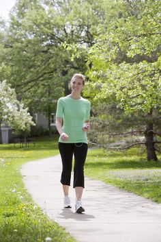 a woman walking down a sidewalk while listening to headphones and holding a water bottle