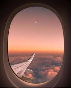 an airplane window with the view of clouds and a crescent in the sky at sunset