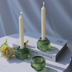 two candles are sitting on a table next to a book and flower arrangement with a rose