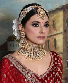 a woman wearing a red and gold bridal outfit with pearls on her head, in front of a painting