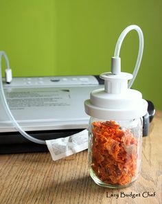 a glass jar filled with dried carrots next to an inkjet machine on a wooden table