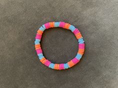 a bracelet made out of colorful beads on top of a gray cloth covered floor with an orange, pink and blue bead in the middle