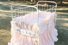 a white crib with pink ruffled sheets in the grass