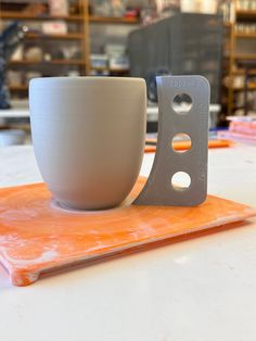 a white cup sitting on top of an orange tray next to a gray cup with holes in it