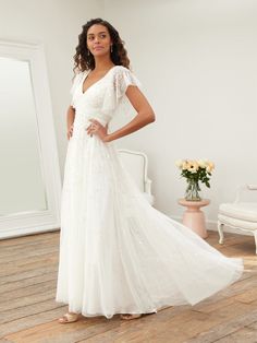 a woman in a white wedding dress standing on a wooden floor next to a mirror