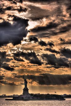 the statue of liberty is silhouetted against an orange and gray sky with clouds above it