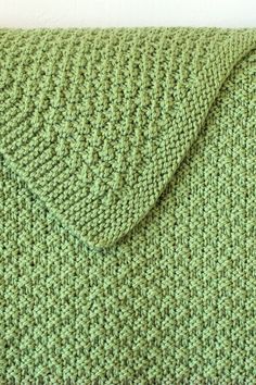 a green knitted blanket laying on top of a white wall