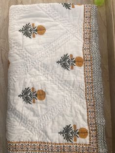 a white quilt with pineapples and leaves on it sitting on top of a table