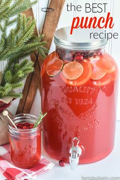 a jar filled with oranges and cranberries next to a christmas tree