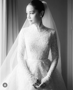 a woman in a wedding dress standing next to a window wearing a veil and holding her hands on her hips