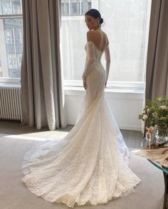 a woman in a wedding dress standing by a window with her hands on her hips